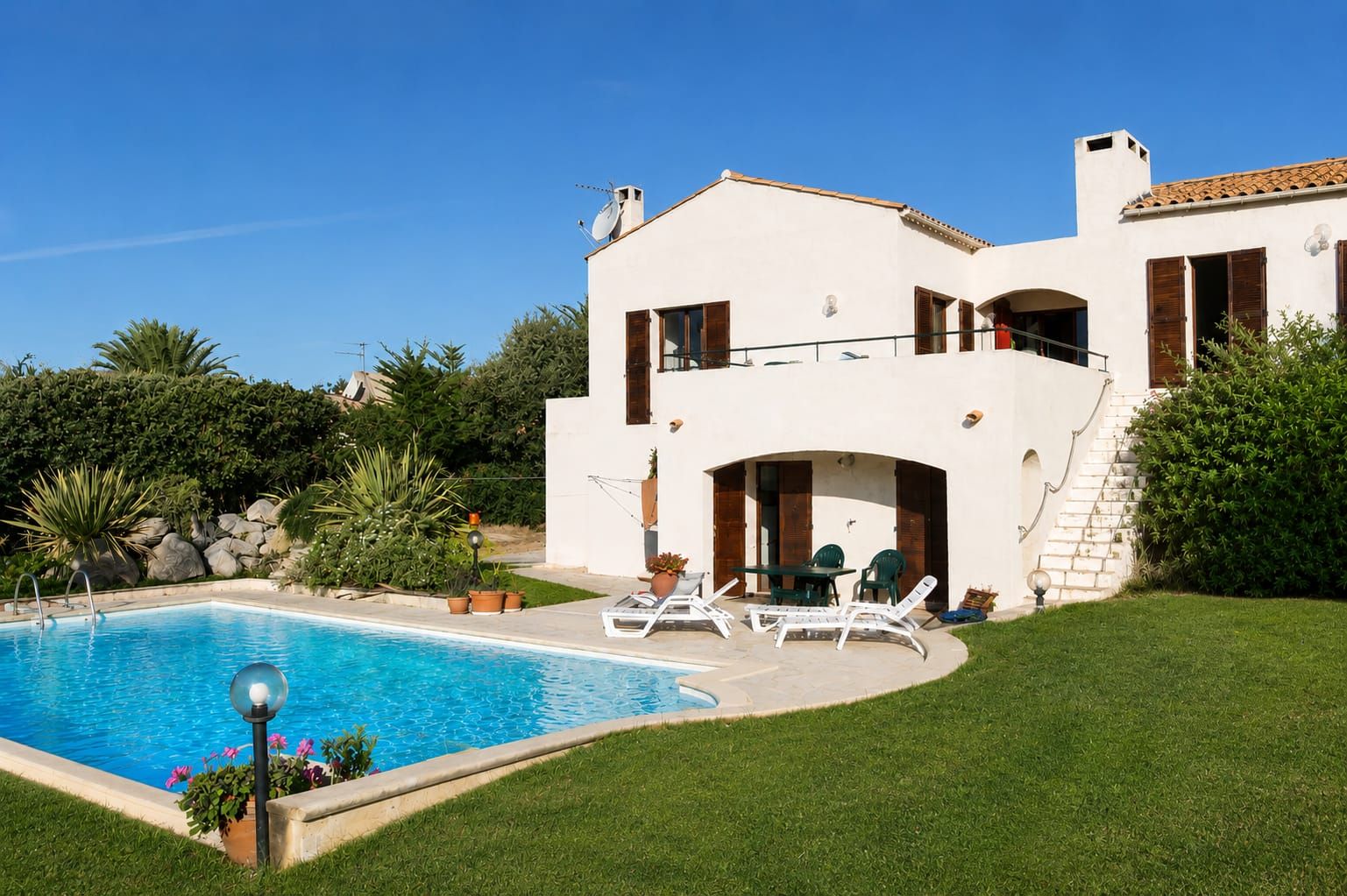 Die Casa di Lumi von außen: weißes Ferienhaus mit Pool, Sonnenliegen, Palmen und Rasen unter blauem Himmel