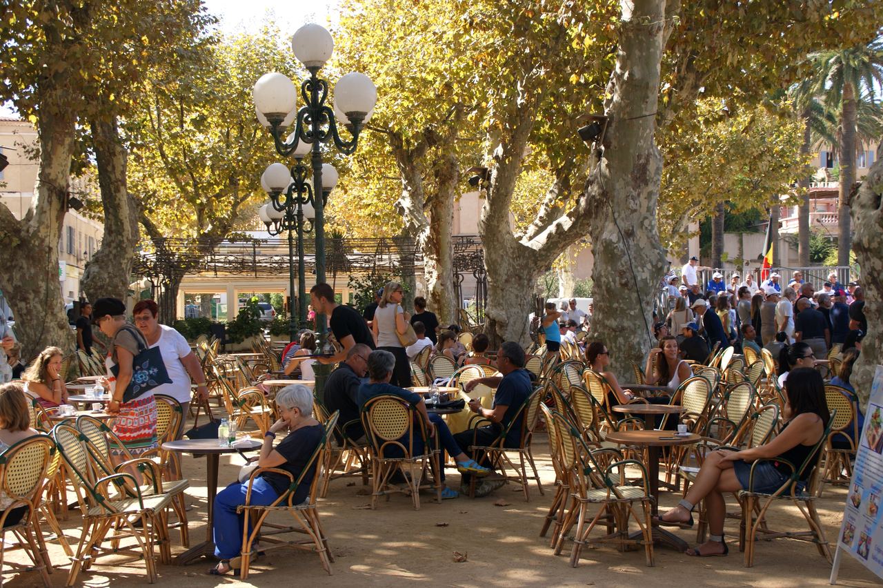 Café-Terrassen unter schattigen Platanen auf dem Marktplatz von L'Île-Rousse mit Gästen