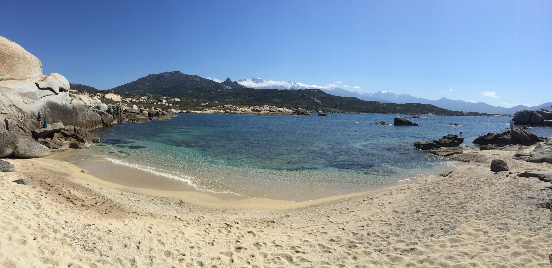 Strand der Balagne mit weißem Sand, türkisem Wasser und Bergpanorama im Hintergrund