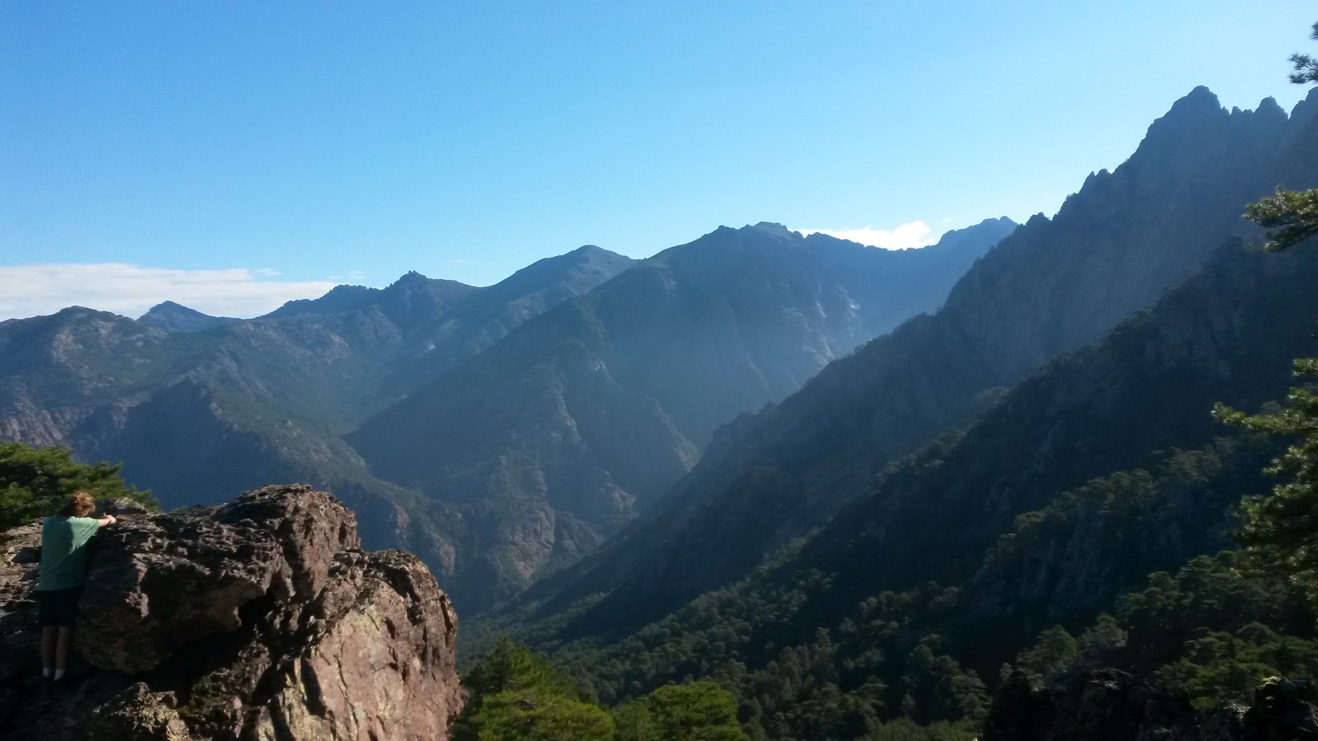 Wanderer auf einem Felsen mit Blick über ein Bergpanorama mit schroffen Granitgipfeln in Korsika